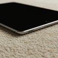 A sleek, silver-colored tablet, likely an iPad, rests on a textured beige surface. The devic Royalty Free Stock Photo