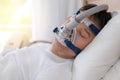 Sleep apnea therapy, Man sleeping in bed wearing CPAP mask.