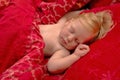 Sleeping blond baby on red bedding, close-up