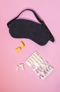 Sleeping eye mask, alarm clock, ear plugs and sleeping pills or vitamins on colourful background.