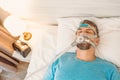 Sleeping man with chronic breathing issues considers using CPAP machine in bed. Royalty Free Stock Photo