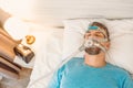 Sleeping man with chronic breathing issues considers using CPAP machine in bed.