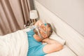 Sleeping man with chronic breathing issues considers using CPAP machine in bed. Royalty Free Stock Photo