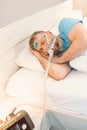 Sleeping man with chronic breathing issues considers using CPAP machine in bed. Royalty Free Stock Photo