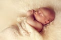 Sleeping newborn baby lying on white fur carpet covered with cream knitted blanket. Royalty Free Stock Photo