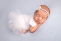 Sleeping newborn girl in a white ballet dress with a white bandage and a blue flower.Portrait of a newborn ballerina. Royalty Free Stock Photo