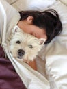 Sleeping with pets: woman cuddling west highland terrier westie Royalty Free Stock Photo