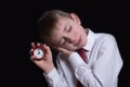 Sleeping schoolboy with a red alarm clock in his hands. Morning concept. Black background. Isolate Royalty Free Stock Photo