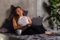 Sleeping woman sitting on bed with a laptop in her lap and white cup aside Royalty Free Stock Photo