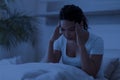 Sleepless black woman sitting in bed alone at night, touching her head Royalty Free Stock Photo