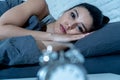 Attractive woman staring at alarm clock trying to sleep feeling stressed depressed and sleepless