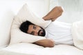 Sleepless young indian man lying in bed and covering ears with pillow Royalty Free Stock Photo
