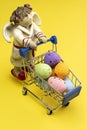 A sleepy Angel carries colorful Easter eggs in a shopping basket