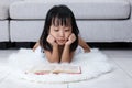 Sleepy Asian Chinese little girl reading book on the floor