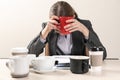 Sleepy businesswoman with a lot of empty cups of coffee sitting at table in office. Concept of addiction