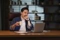 Sleepy employee sitting at dark office, using laptop, drinking coffee