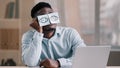 Sleepy funny african american office manager business man sitting at home workplace with sticky notes on eyes comic Royalty Free Stock Photo