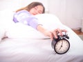 Sleepy girl in bed with eyes closed Reach out to the alarm clock at home. Good morning on a lazy day Royalty Free Stock Photo