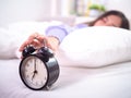 Sleepy girl in bed with eyes closed Reach out to the alarm clock at home. Good morning on a lazy day Royalty Free Stock Photo