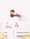 Sleepy guy frowning and raising his eyebrows. Man in bathrobe standing in front of piano. Tired hipster in his apartment