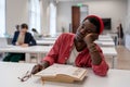 Sleepy lazy African American man falls asleep sits in library with head resting on desk with books Royalty Free Stock Photo