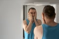 Sleepy man in bathroom looks at himself in mirror. Male touching his beard and face. Morning rituals Royalty Free Stock Photo