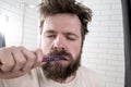A sleepy man with his eyes closed, disheveled hair and a thick beard is brushing his teeth with a toothbrush, in the early morning Royalty Free Stock Photo