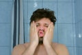 Sleepy shaggy young man with headache in bathroom in morning rubs his face. Royalty Free Stock Photo