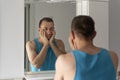 Sleepy tired man in bathroom looks at himself in mirror. Male touching his beard and face. Morning routine Royalty Free Stock Photo