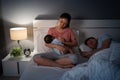 sleepy and tired mother breastfeeding newborm baby while her husband sleeping on bed at night Royalty Free Stock Photo