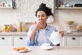 Sleepy tired woman waking up early, pouring tea into cup and yawning, sitting in modern kitchen interior, copy space Royalty Free Stock Photo