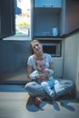 Sleepy tired woman sitting kitchen floor at night and feeding her baby boy with milk