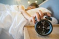 Sleepy woman in bed switching off alarm clock