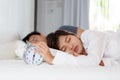 Sleepy woman turn off alarm clock beside a man in the morning.