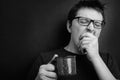 Sleepy yawning man in eyeglasses with red cup of tea or coffee has uncombed hair in underwear on black background, morning refresh Royalty Free Stock Photo