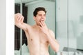 Sleepy yawning naked man standing in home