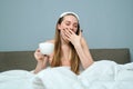 Sleepy yawning young woman in bed with cup of tea