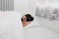 Sleepy young Asian man with blindfold eye mask comfortably sleeping on the white bed in bedroom Royalty Free Stock Photo
