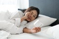 Sleepy young Asian woman lying in bed turning off an alarm clock in the morning Royalty Free Stock Photo