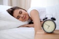 Sleepy young brunette woman stretching hand to ringing alarm willing turn it off. Early wake up, not getting enough