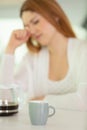 Sleepy young female rubbing facewith coffee in foreground