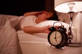 Sleepy young man in bed with extending hand to alarm clock in morning Royalty Free Stock Photo