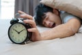 Sleepy young man in bed with eyes closed extending hand to alarm Royalty Free Stock Photo