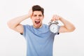 Sleepy young man 30s with brown hair holding alarm clock and yaw Royalty Free Stock Photo