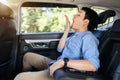 Sleepy man yawning while sitting in the back seat of car