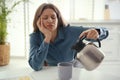 Sleepy young woman pouring coffee into cup at home in morning