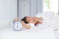 Sleepy young woman stretching hand to trying kill alarm clock in Royalty Free Stock Photo