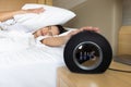 Sleepy young woman trying kill alarm clock while bury hand in pillow Royalty Free Stock Photo