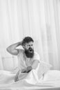 Sleepyhead concept. Guy on sleepy tired face yawning. Man in shirt yawning while sit on bed, white curtain on background Royalty Free Stock Photo