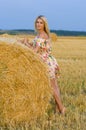 Vertical portrait of a young slender blonde near a haystack on a background of sky and field